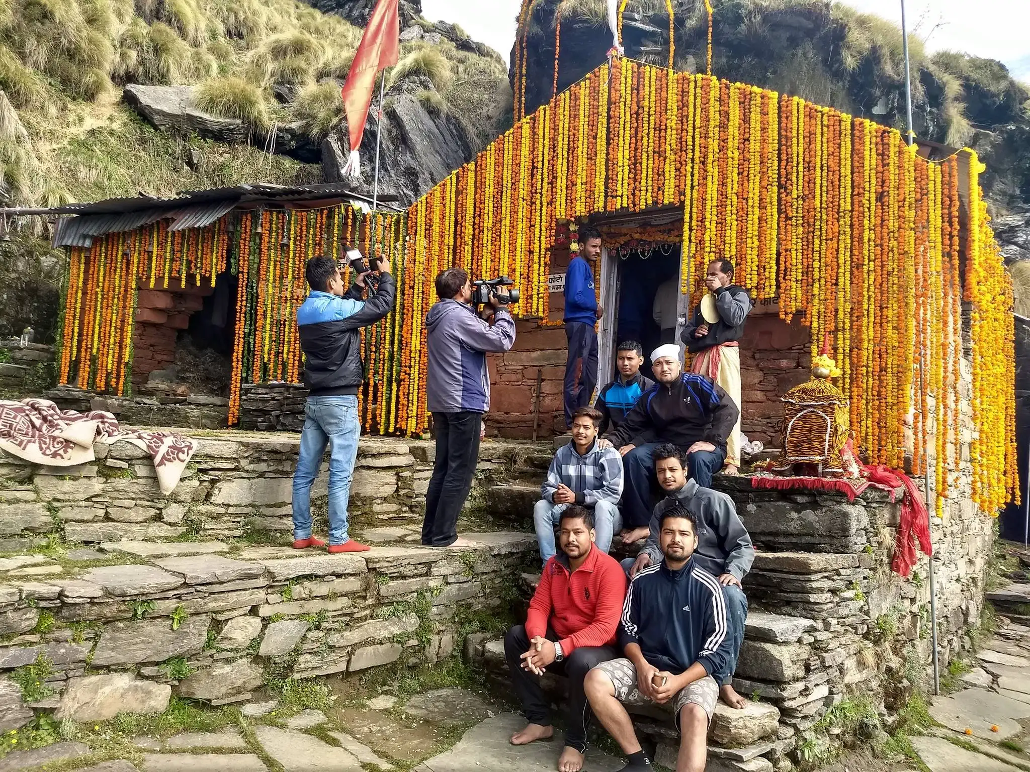 Rudranath temple decorated with garlands of marigold, with pilgrims seated on the stone steps in front