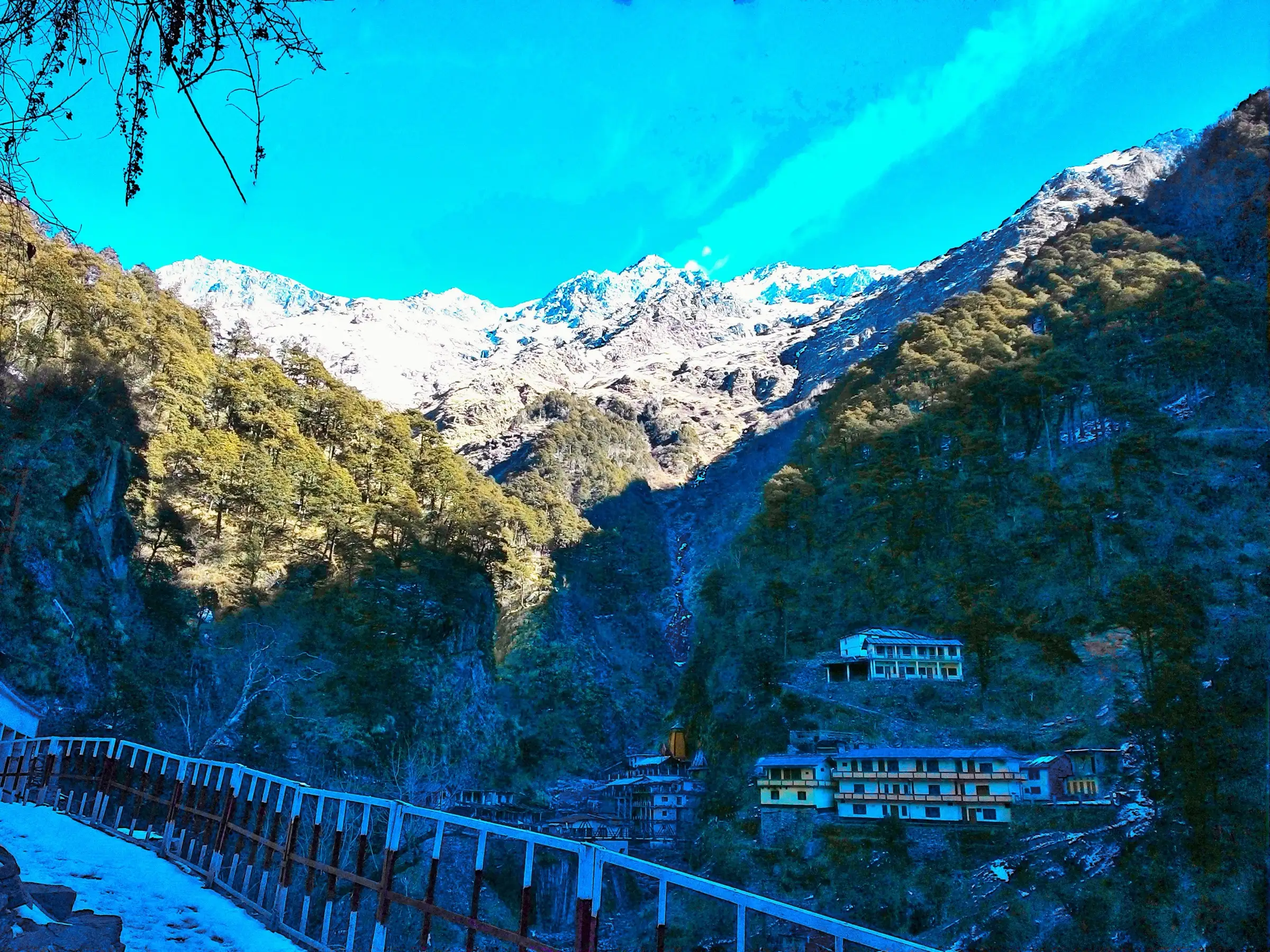 Yamunotri Dham and its lodges in a forested gorge below the snow-covered ridge that the Saptarishi Kund route climbs towards