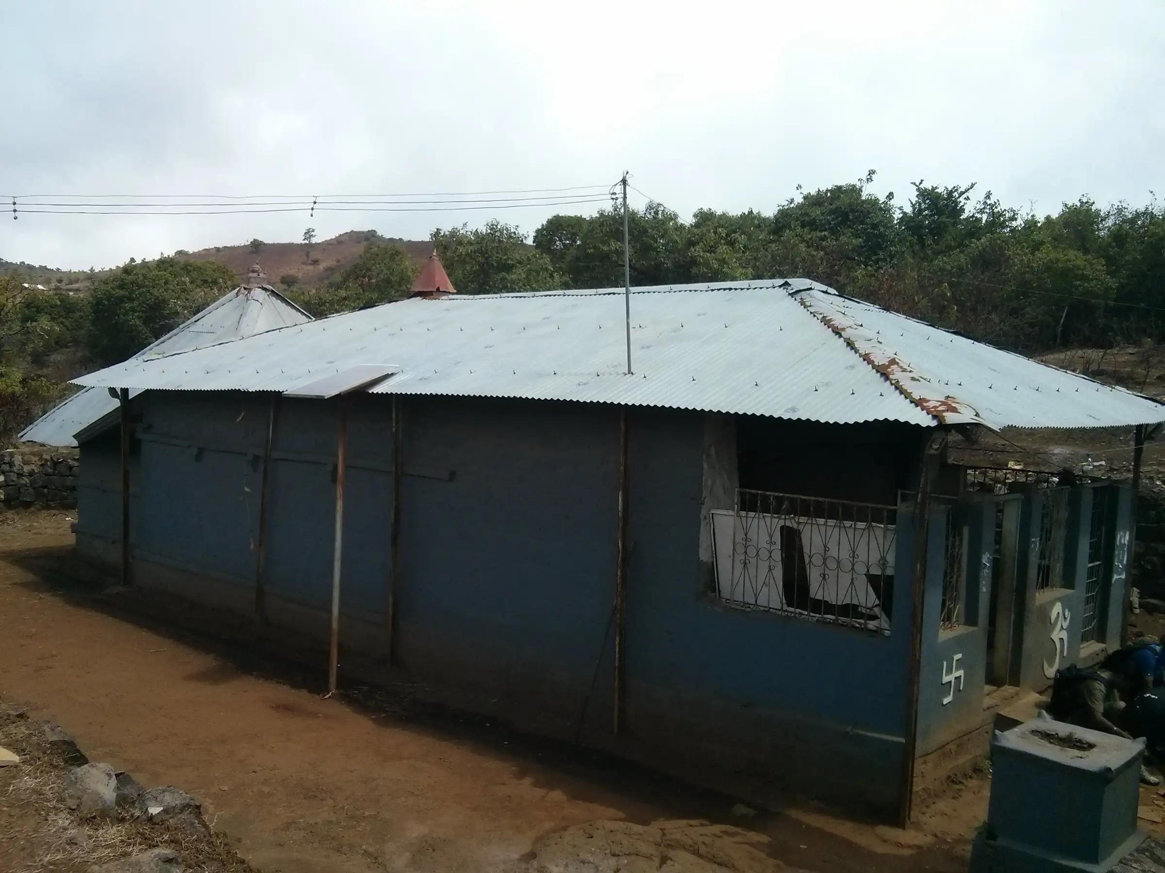 Shri Raireshwar Mandir on the plateau, a low stone temple with a tin roof, Om and swastika painted beside the entrance