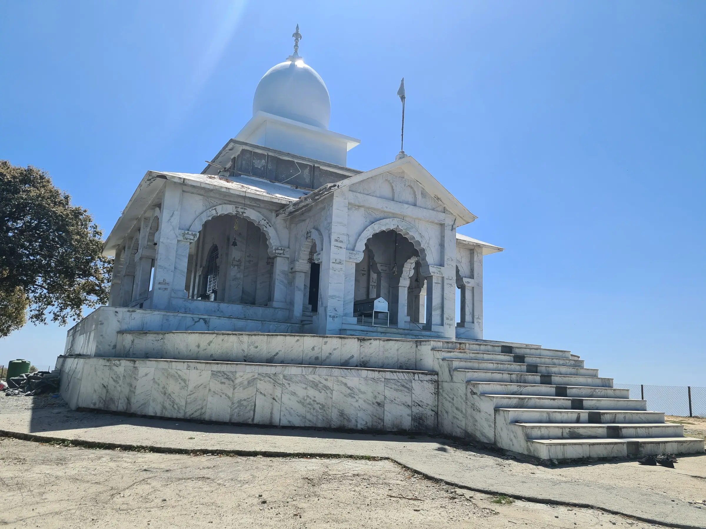 White marble Bhadraj Temple with its dome and arched porch on the bare hilltop under a clear blue sky