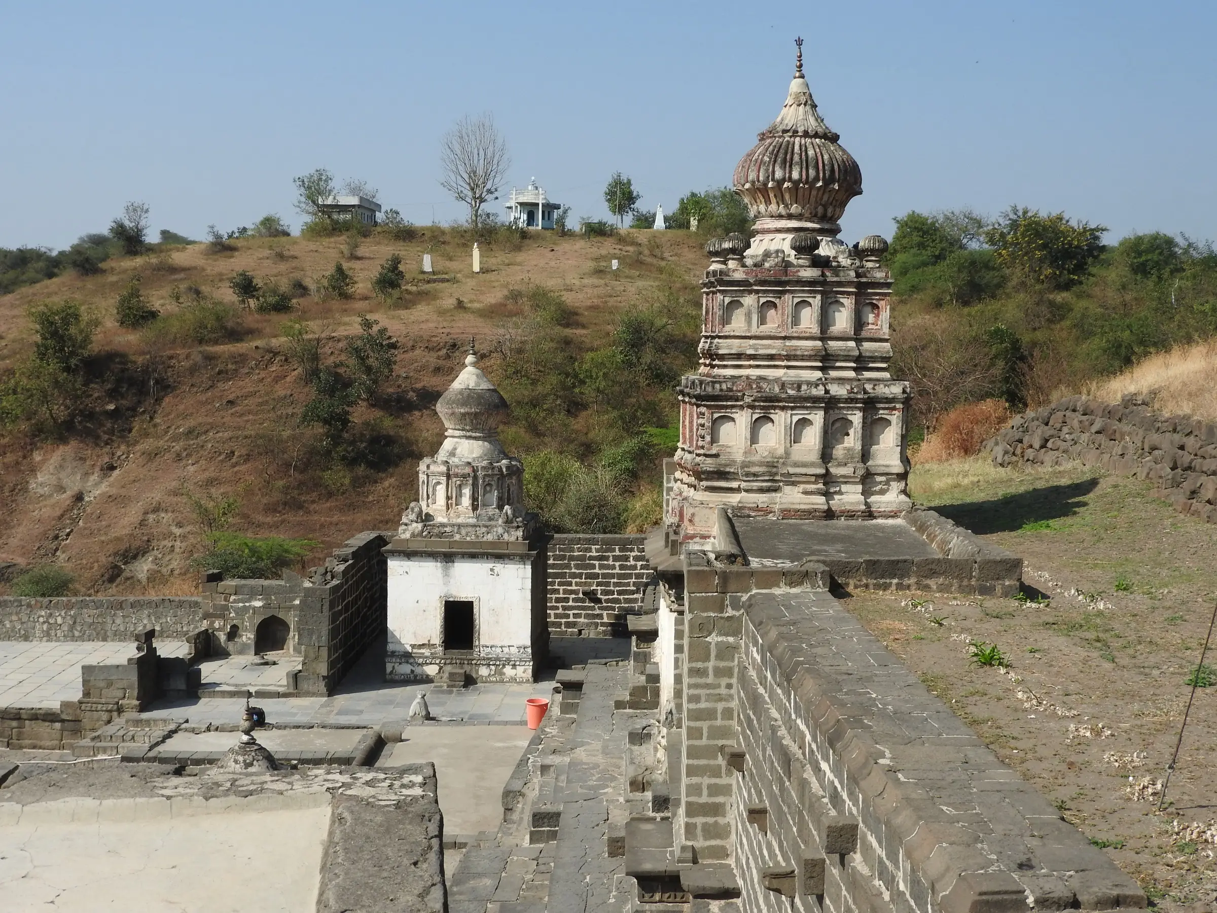 Old stone temples with carved shikharas inside a walled complex on the slope of Lonar crater