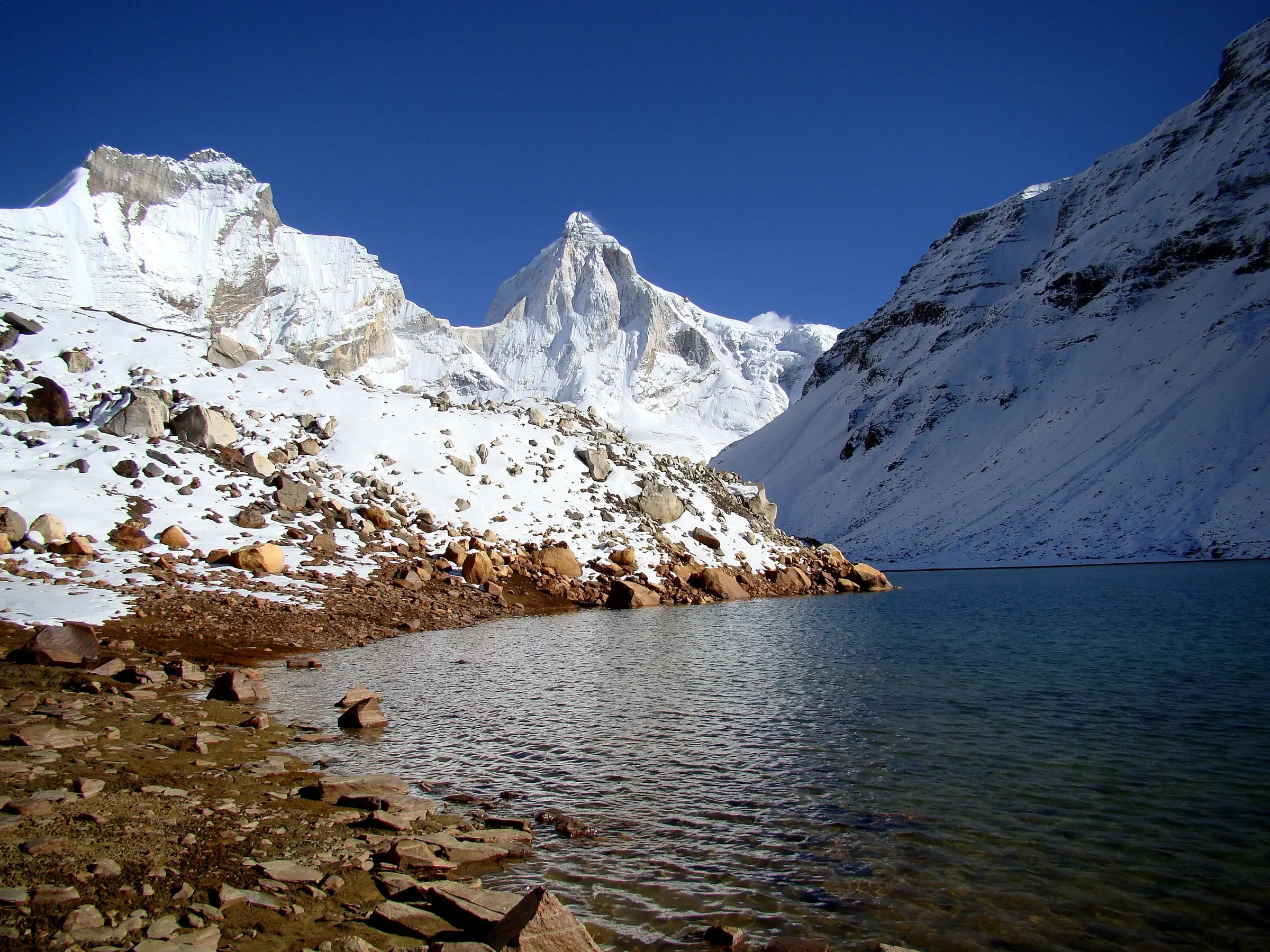Kedartal lake with a rocky shore below the snow-covered pyramid of Thalay Sagar under a deep blue sky