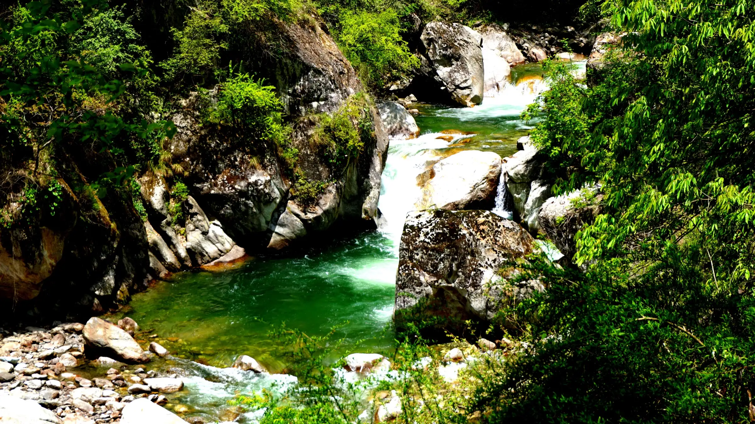 Green pools and small cascades of the Tirthan river between boulders, just before the entry gate of the Great Himalayan National Park