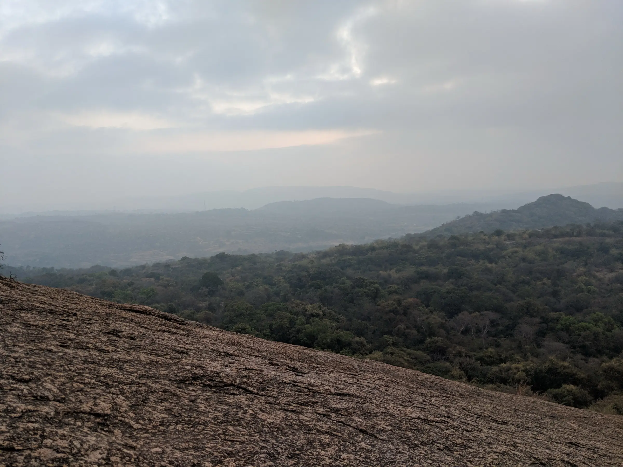 Granite slope near the top of Savandurga looking over forested hills in morning haze