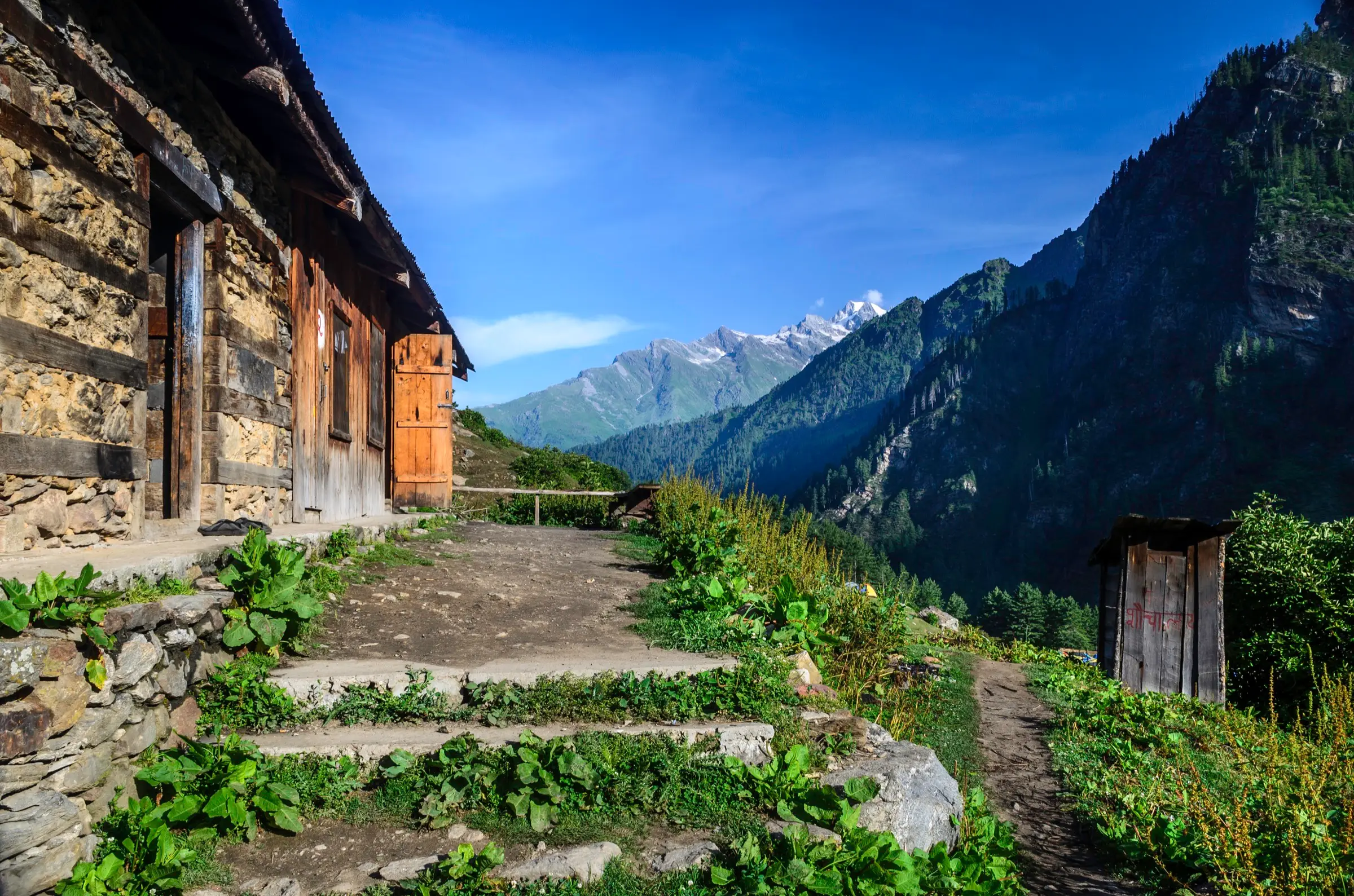 Stone hut and steps at Kheerganga with snow peaks above the Tosh glacier valley in the distance, near the trek