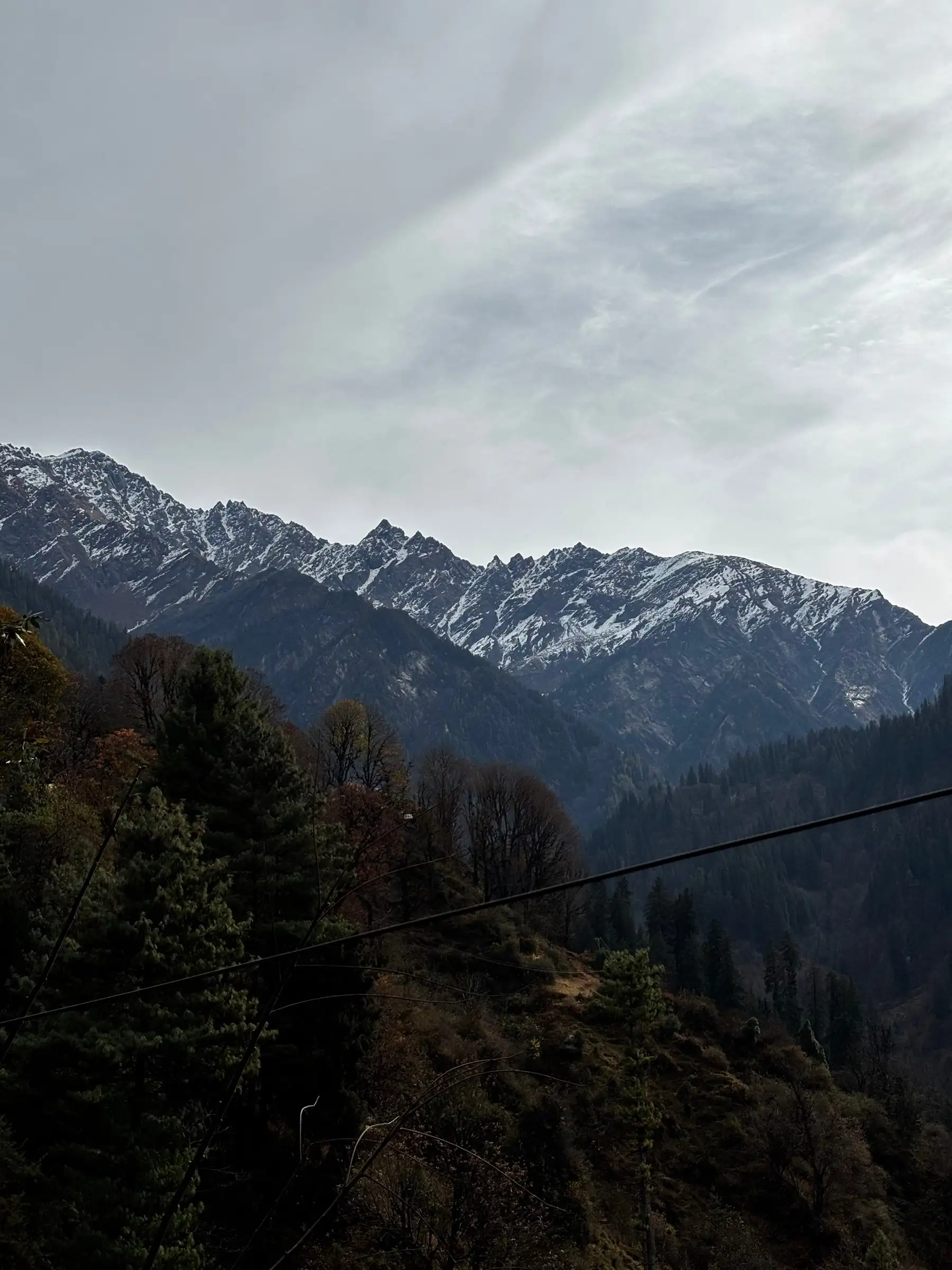Forested slope and a snow-dusted rocky ridge under cloud, between Tosh and Kutla villages