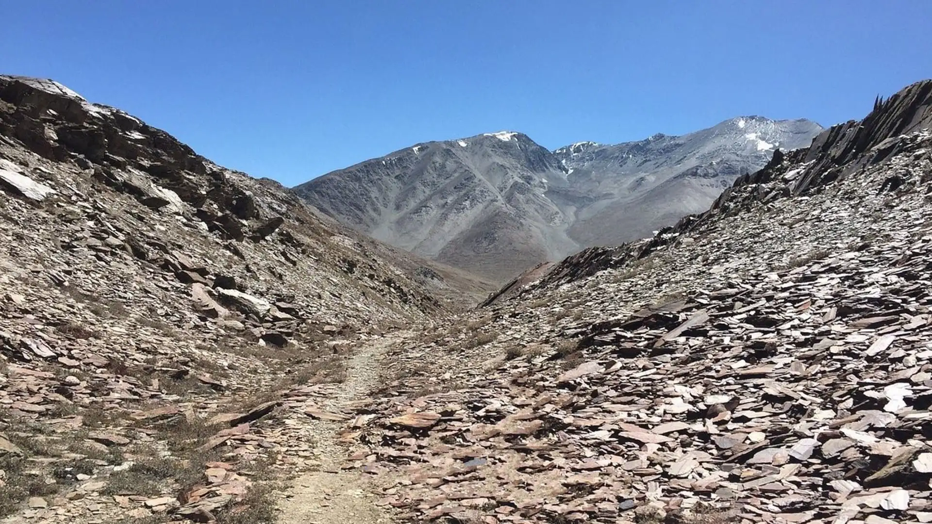 Narrow dirt path through slate scree on the climb to Dhankar Lake, with bare grey mountains ahead