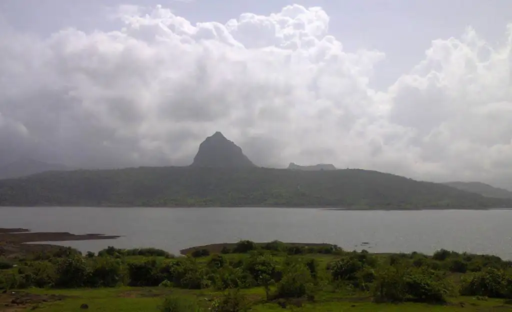 The pointed peak of Tung Fort under monsoon clouds, seen across the Pawna reservoir