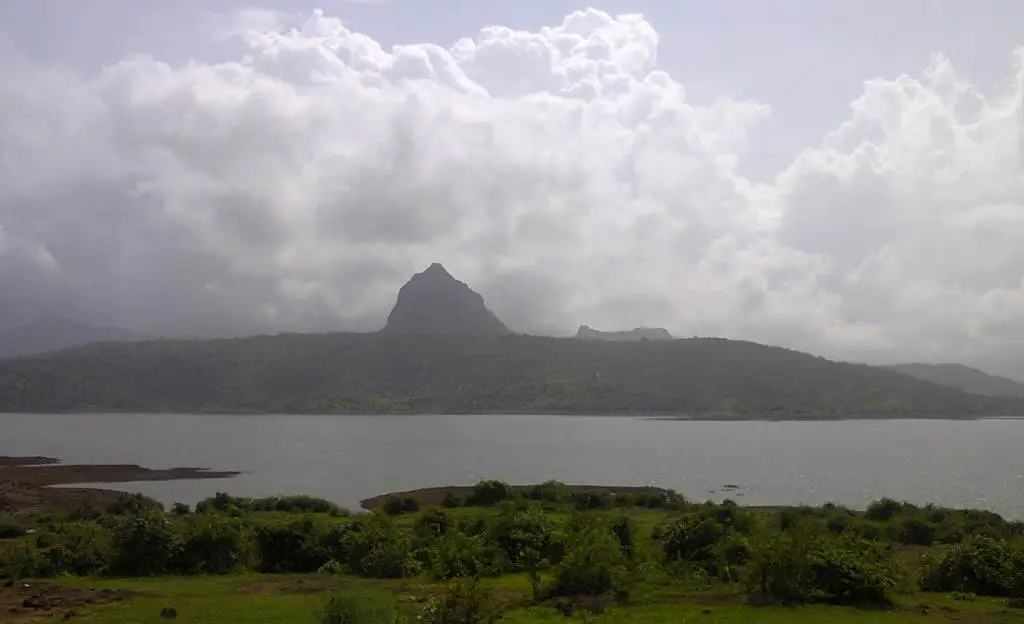 The pointed peak of Tung Fort under monsoon clouds, seen across the Pawna reservoir