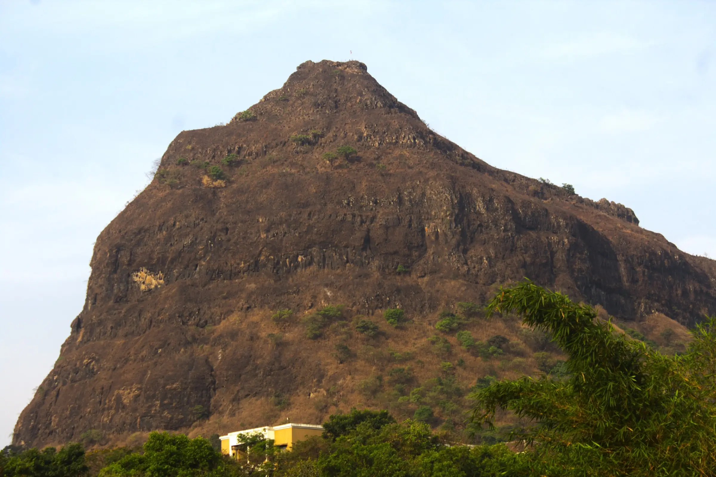 The steep, conical rock face of Tung Fort rising above trees in dry-season sunlight, with a flag on the summit