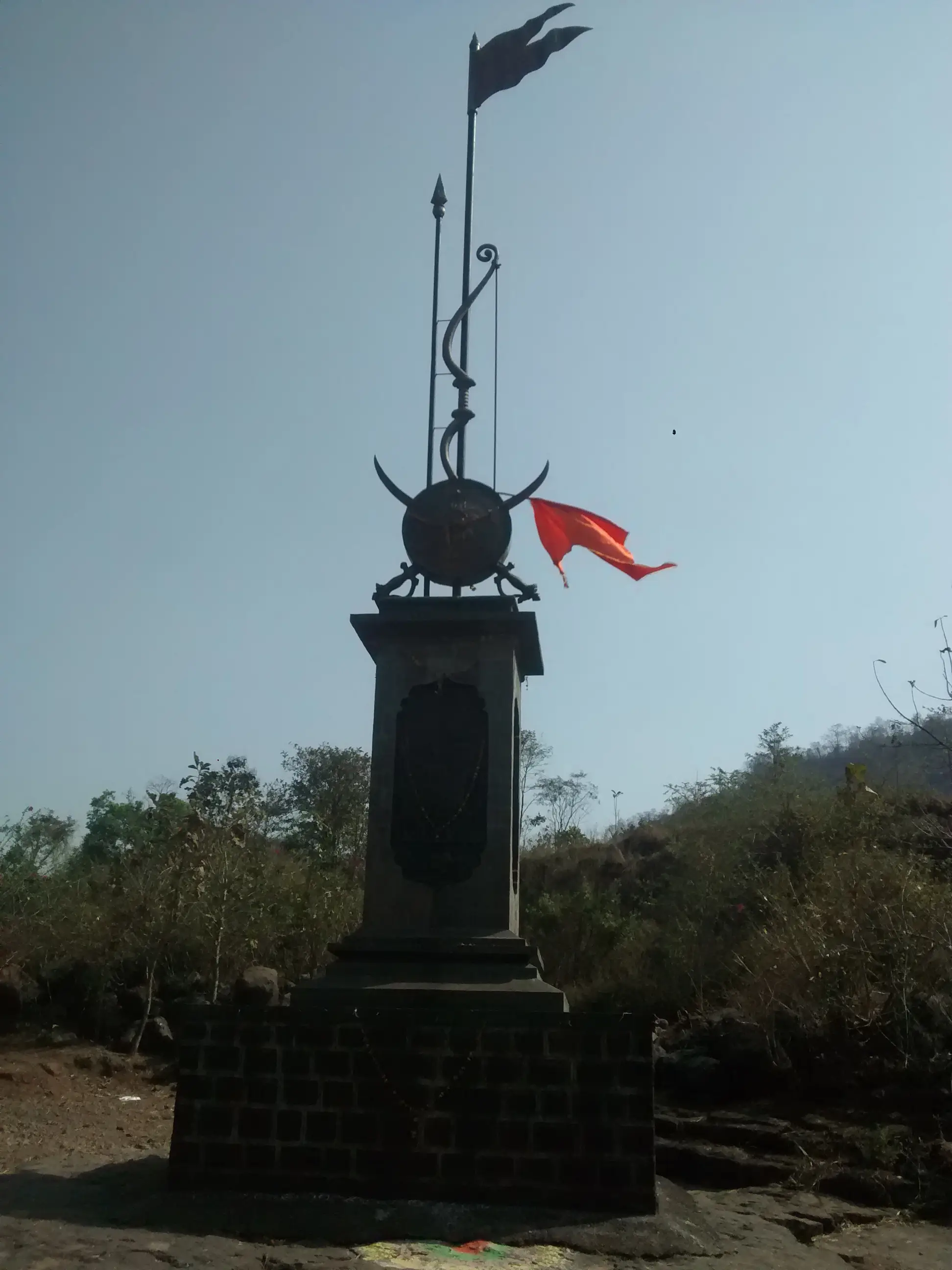 Umberkhind memorial pillar with a saffron flag on rocky ground under a clear dry-season sky