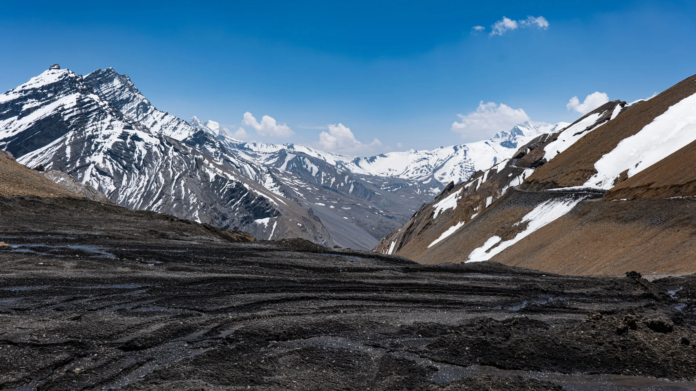 Unta Dhura pass seen from Khingur Dhura, with snow-streaked peaks, a scree slope and a track cut across the mountainside