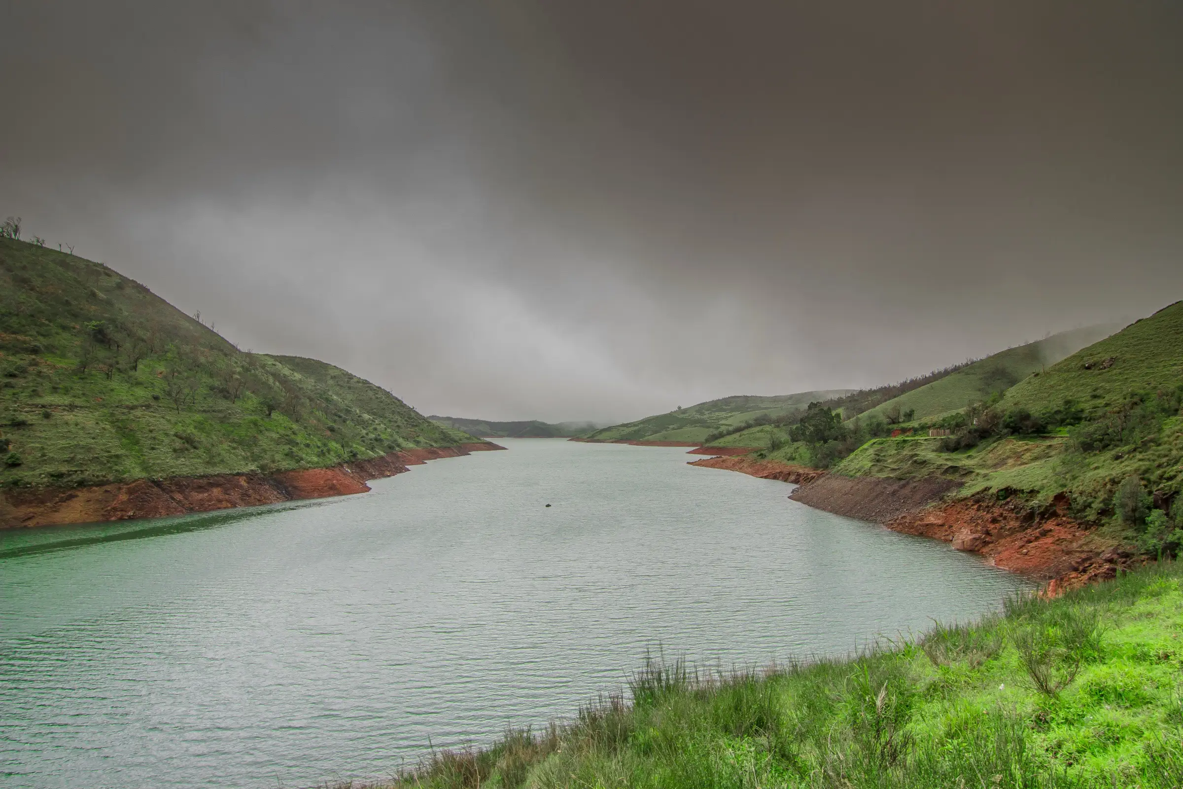 The Upper Bhavani reservoir between green grassy hills under monsoon clouds, the lake seen on the Kolaribetta trek (photo taken near the trek, not on it)