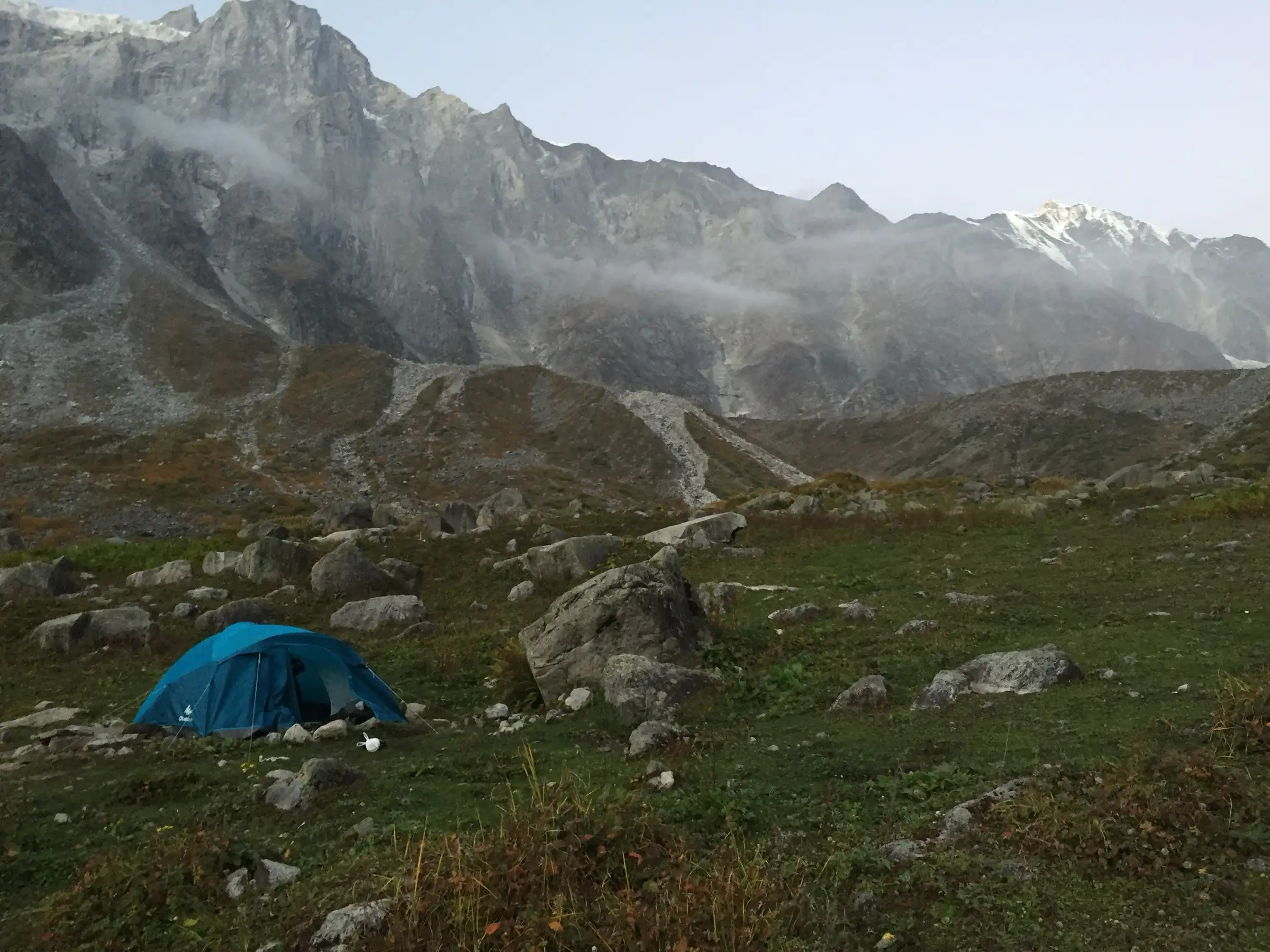 A blue tent on a boulder-strewn meadow below grey cliffs near Lady Leg, on the shared Beas Kund and Friendship Peak route