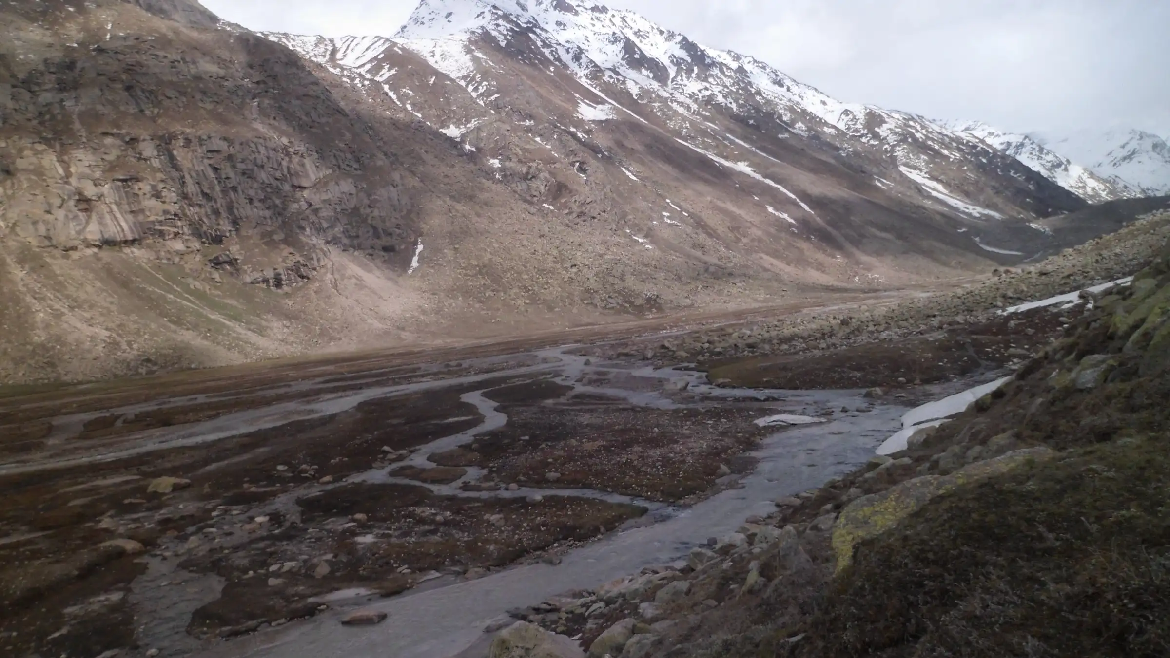 Braided glacial streams across a wide flat valley floor near Mantalai, below snow-dusted mountains
