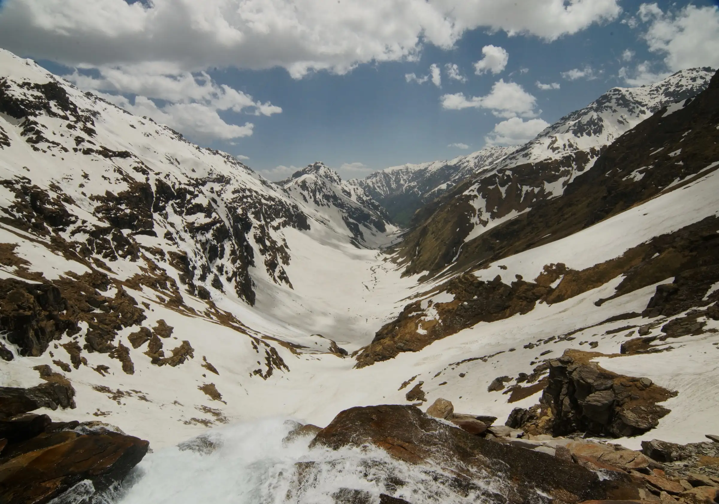 View from the top of the Rupin waterfall down a snow-filled valley between rocky mountainsides