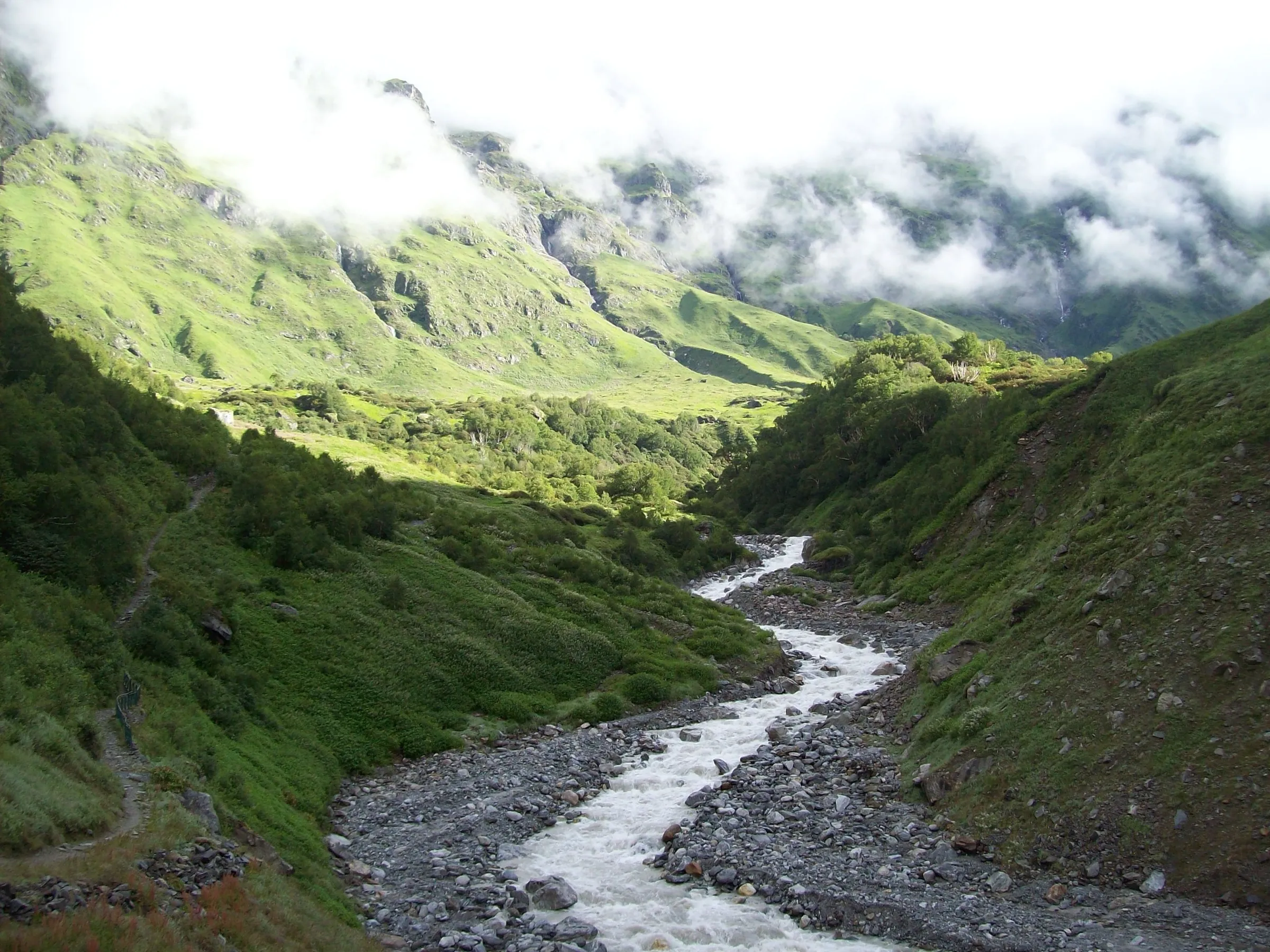 Green slopes of the Valley of Flowers in the upper Bhyundar valley with the Pushpawati stream and low cloud on the ridges