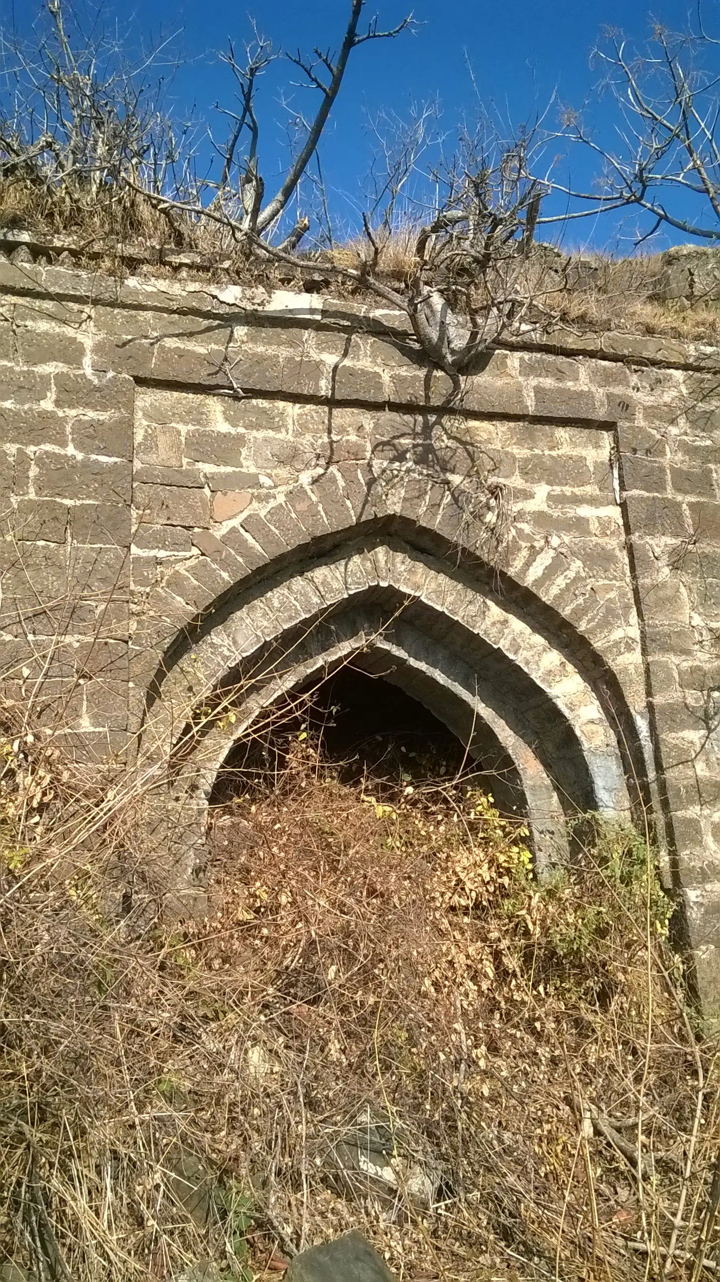 Pointed stone archway of a gate on Vandan Fort, half choked with dry scrub