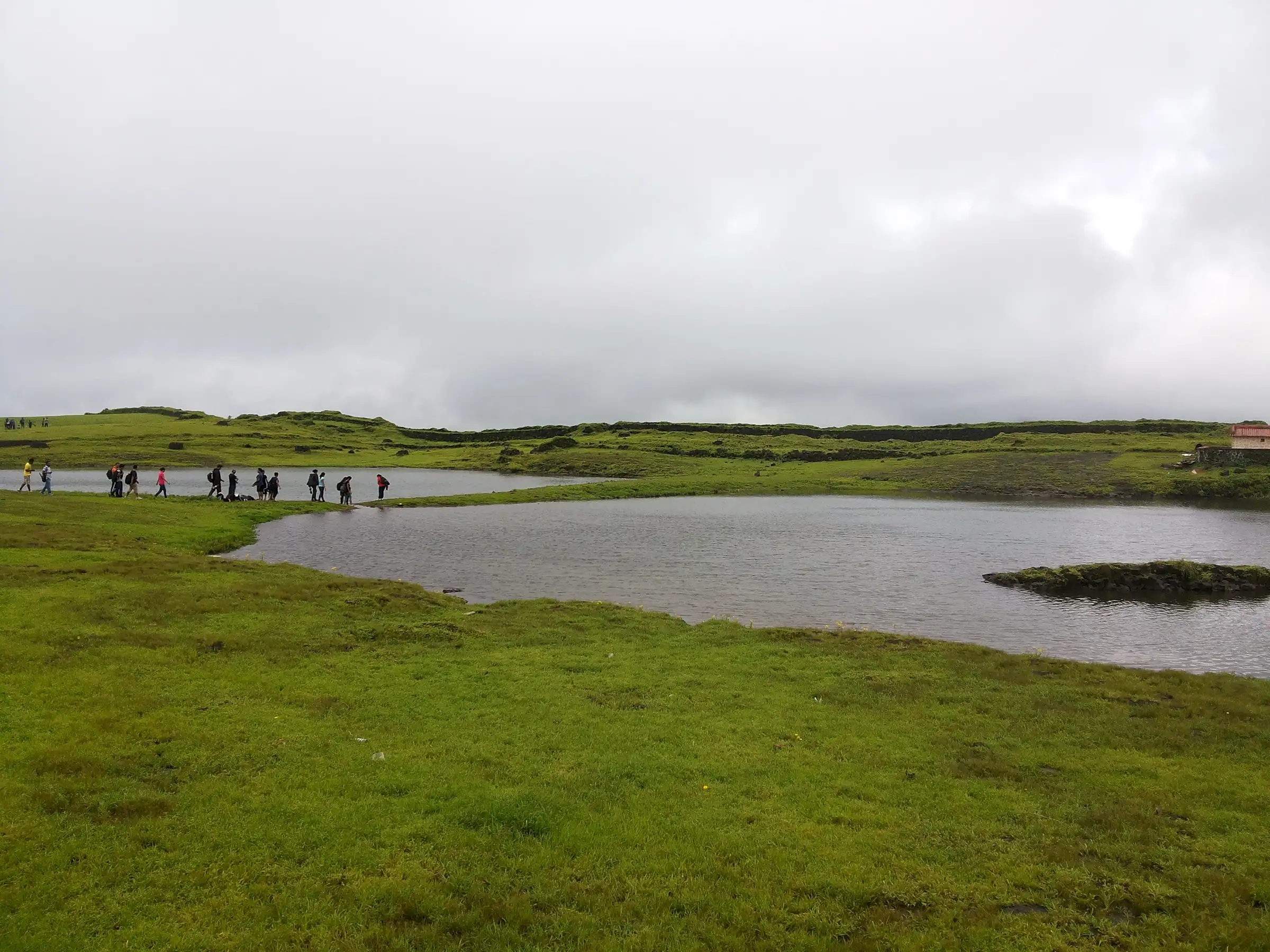 Trekkers walking past one of the lakes on the flat grassy top of Korigad on a cloudy monsoon day