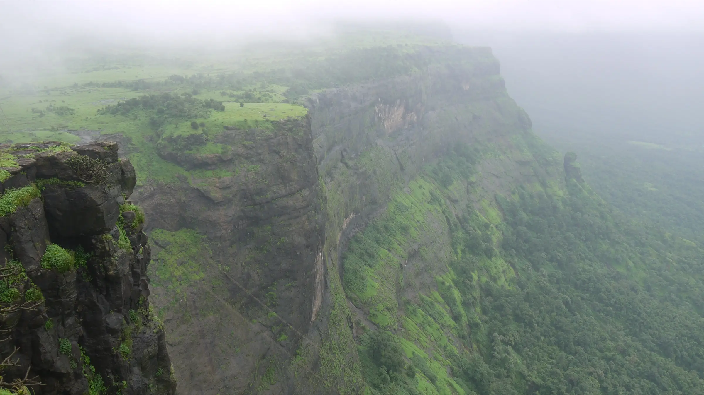 Misty view from the top of Naneghat along a long green escarpment dropping to forest below