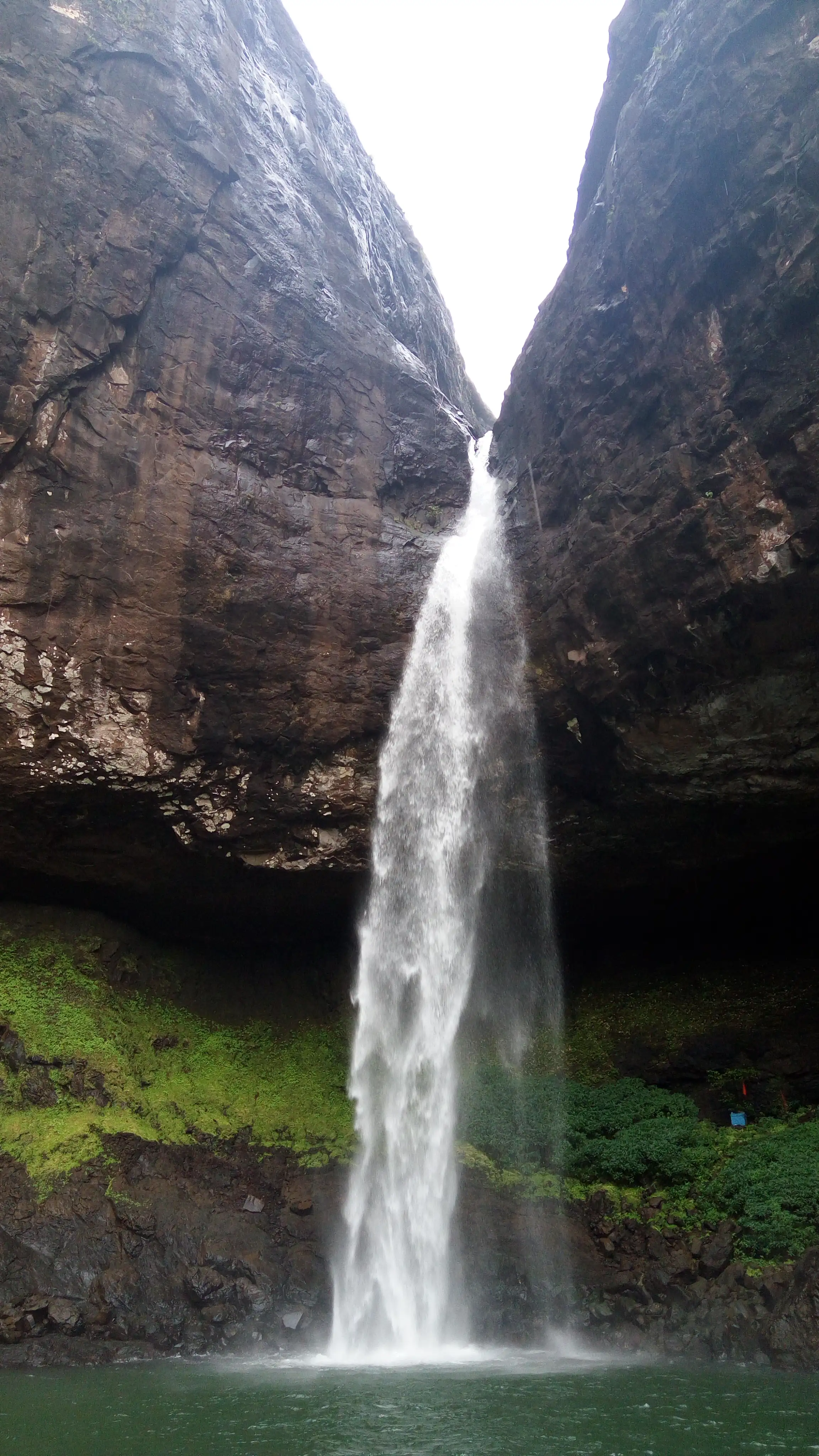 Devkund Waterfall dropping between dark rock walls into a green pool