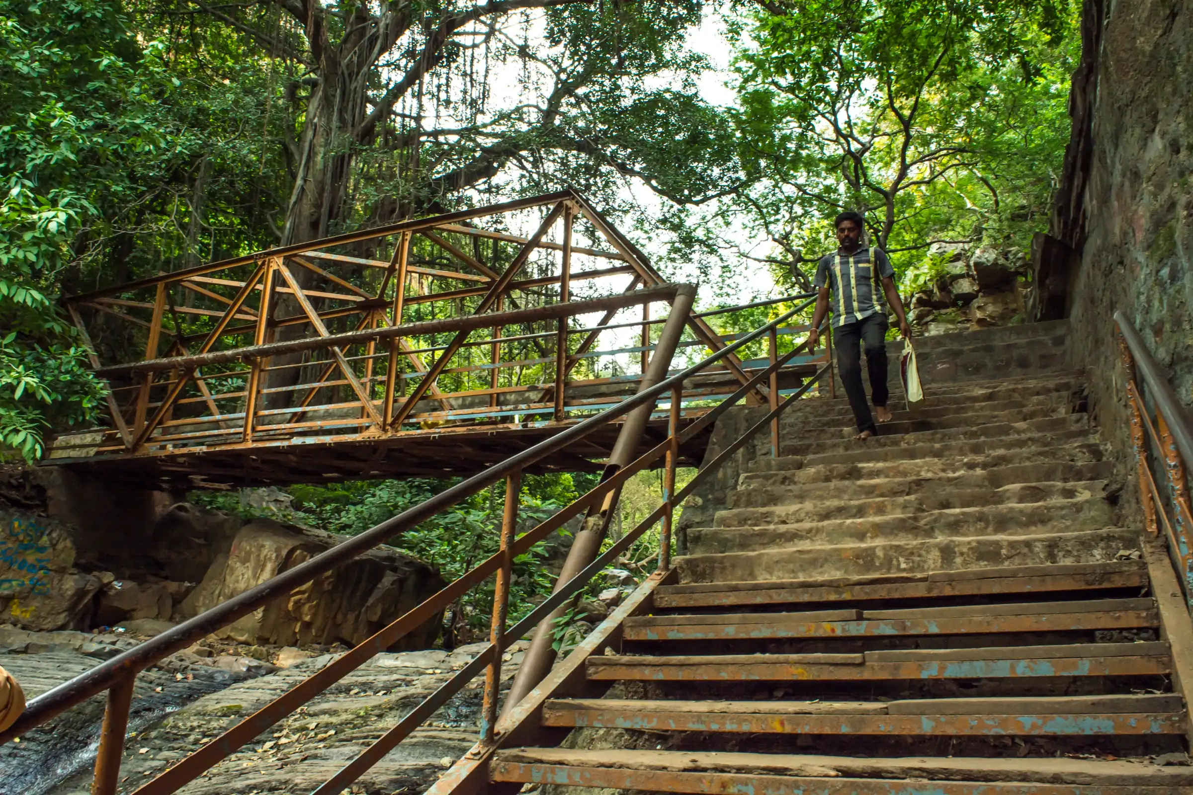 Stone steps with iron railings and a steel footbridge over the rocky stream on the way to Jwala Narasimha temple