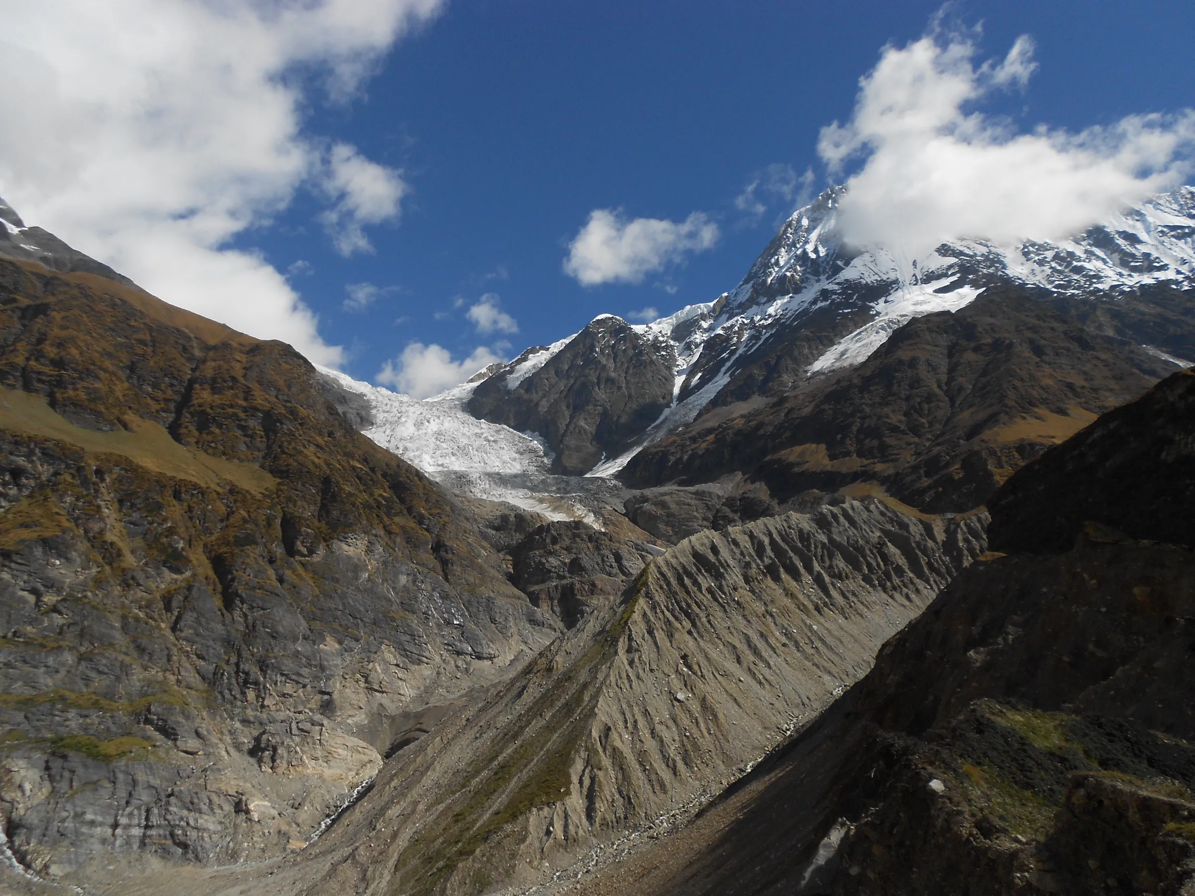 The white tongue of the Pindari Glacier between snow-capped rock peaks, seen from Zero Point above a deep grey moraine valley