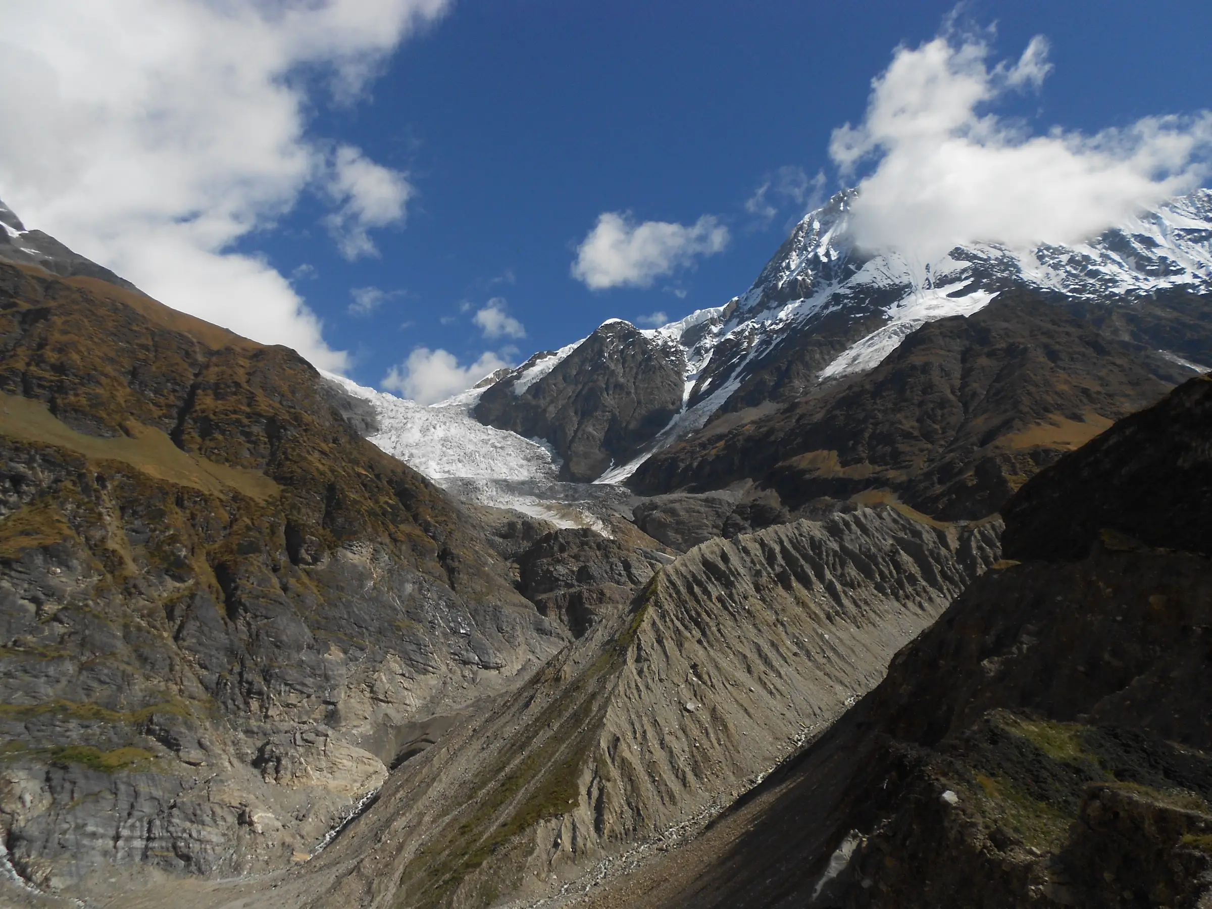 The white tongue of the Pindari Glacier between snow-capped rock peaks, seen from Zero Point above a deep grey moraine valley on the approach to the pass